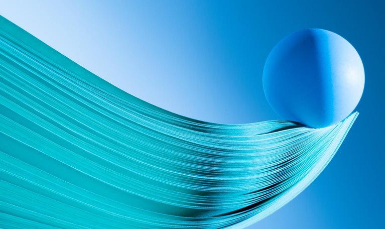Close up of multiple sheets of green tinted paper in curve shape, blue ball balance at tip
