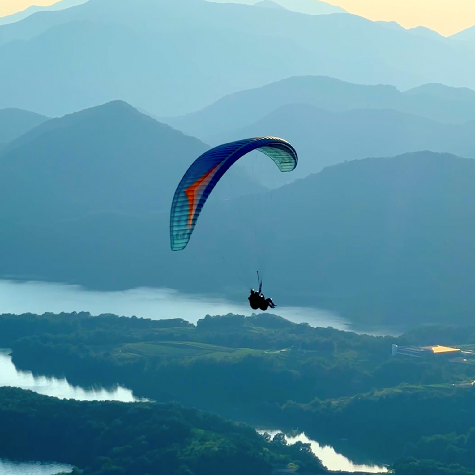 A person paraglides on high mountains overlooking the lake