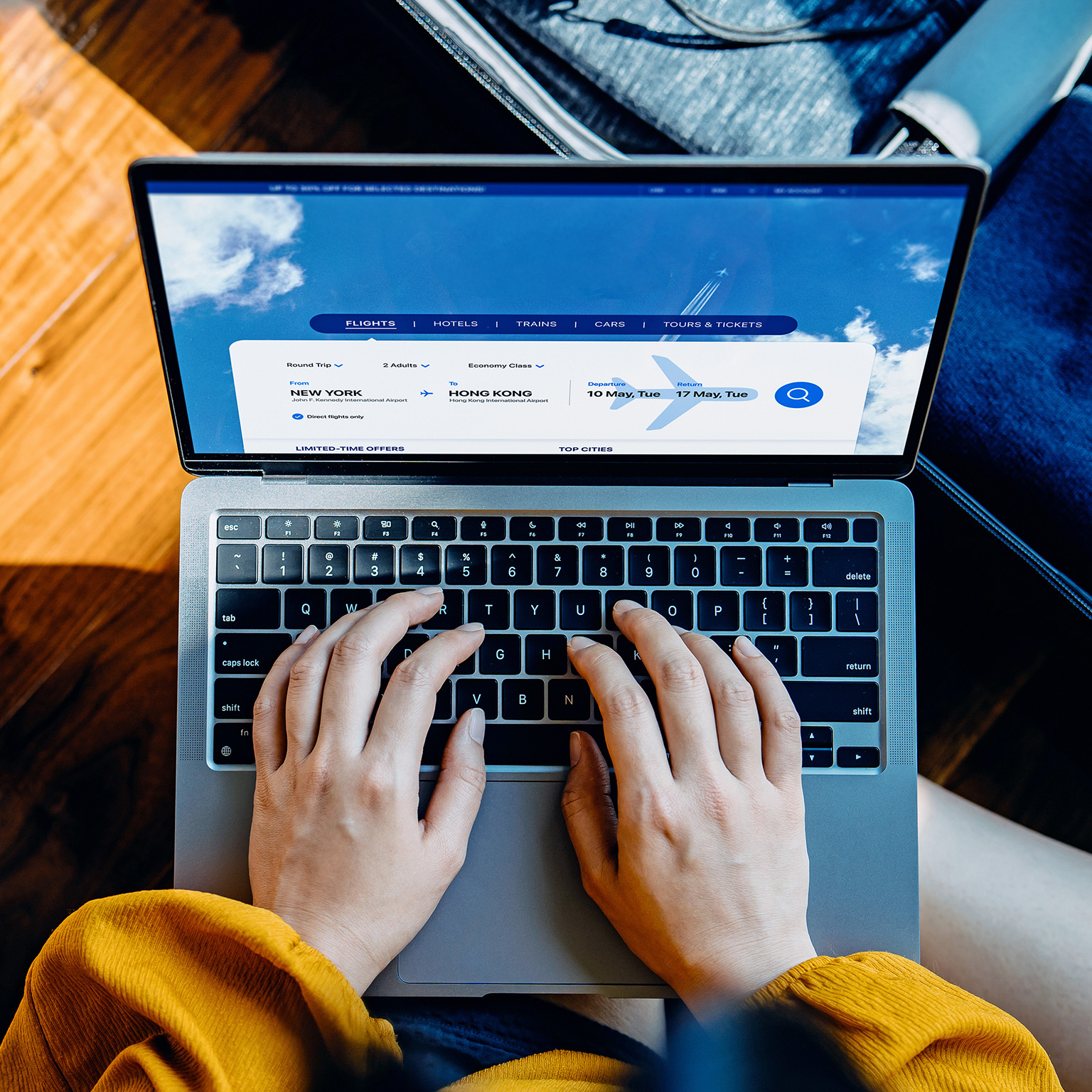 High angle shot of young woman booking flight tickets on airline website with her laptop, a packed suitcase by her side. 
